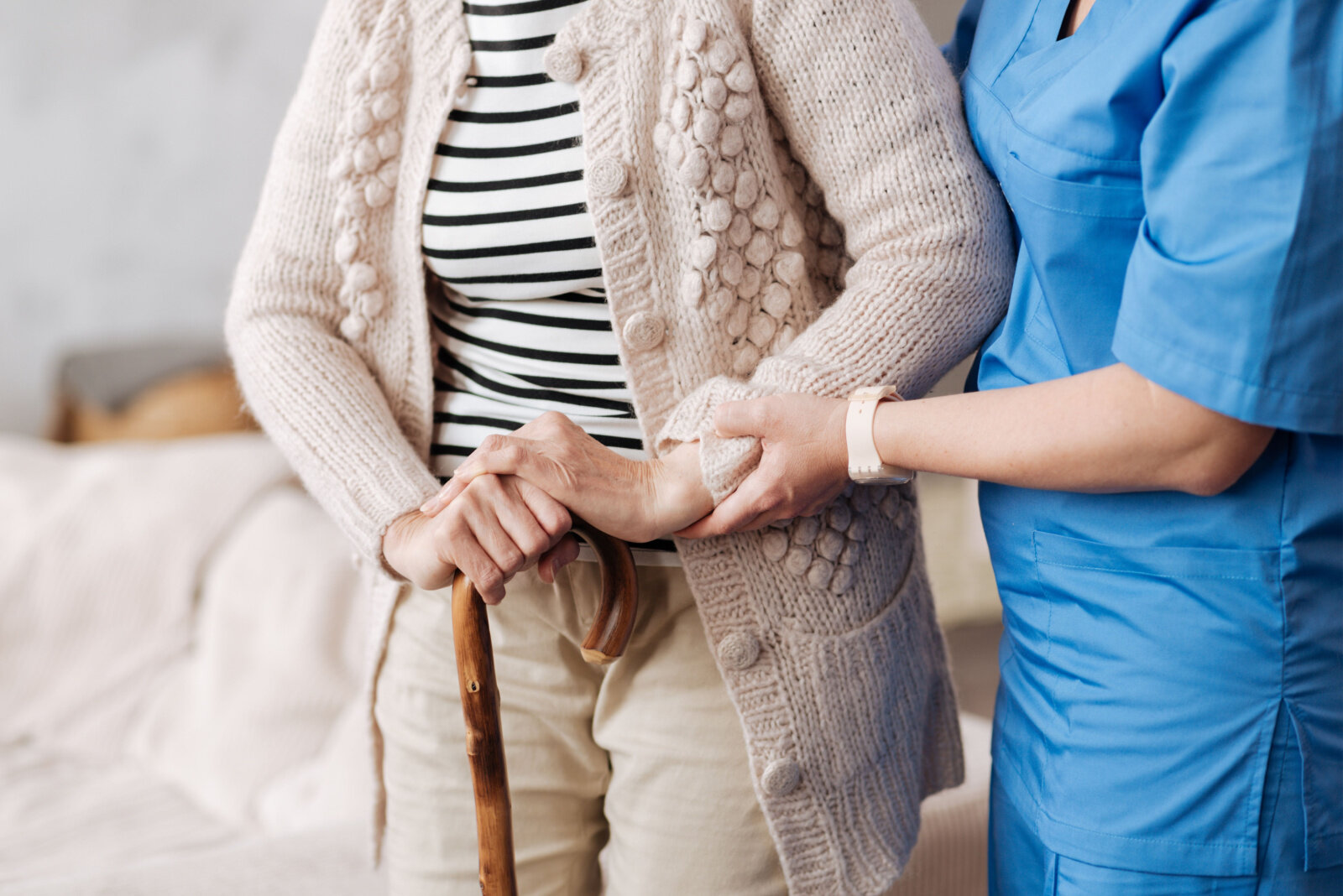 A respite care professional is helping an elderly patient stand on her feet.
