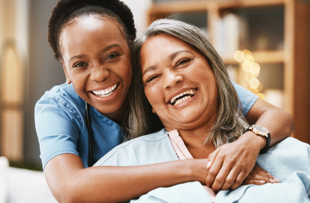 A caregiver and a senior woman smiling while looking directly at the camera.