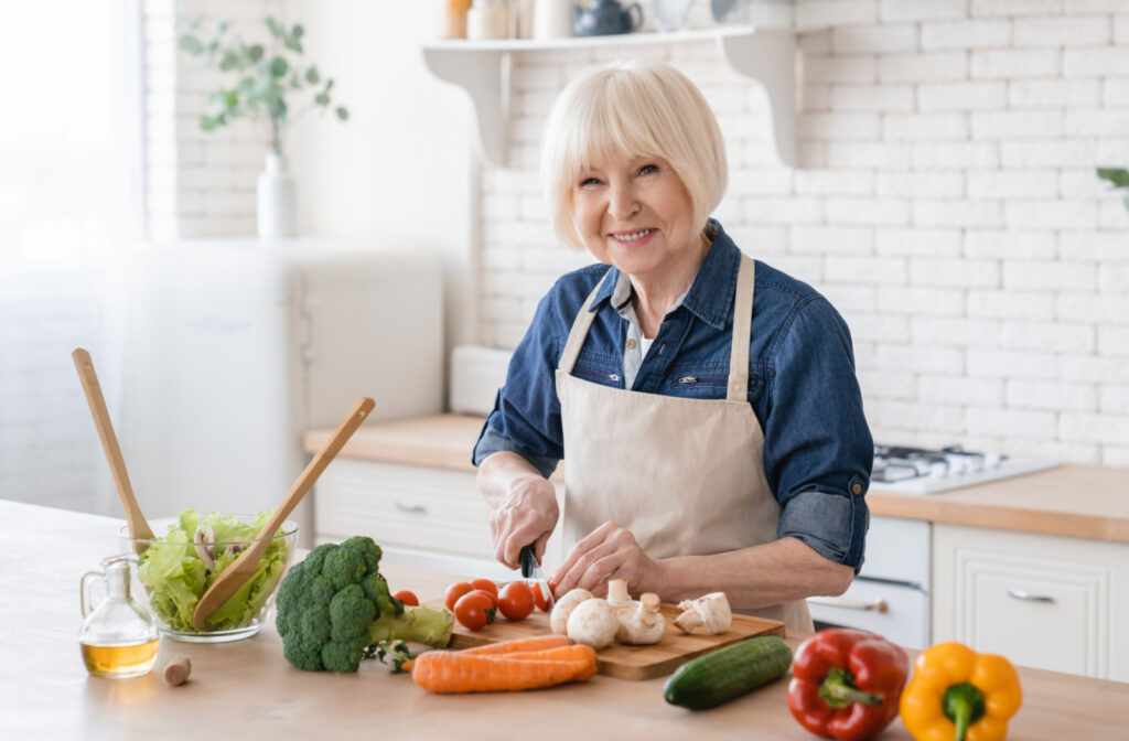 A senior woman with gray hair cutting vegetables and preparing a salad.