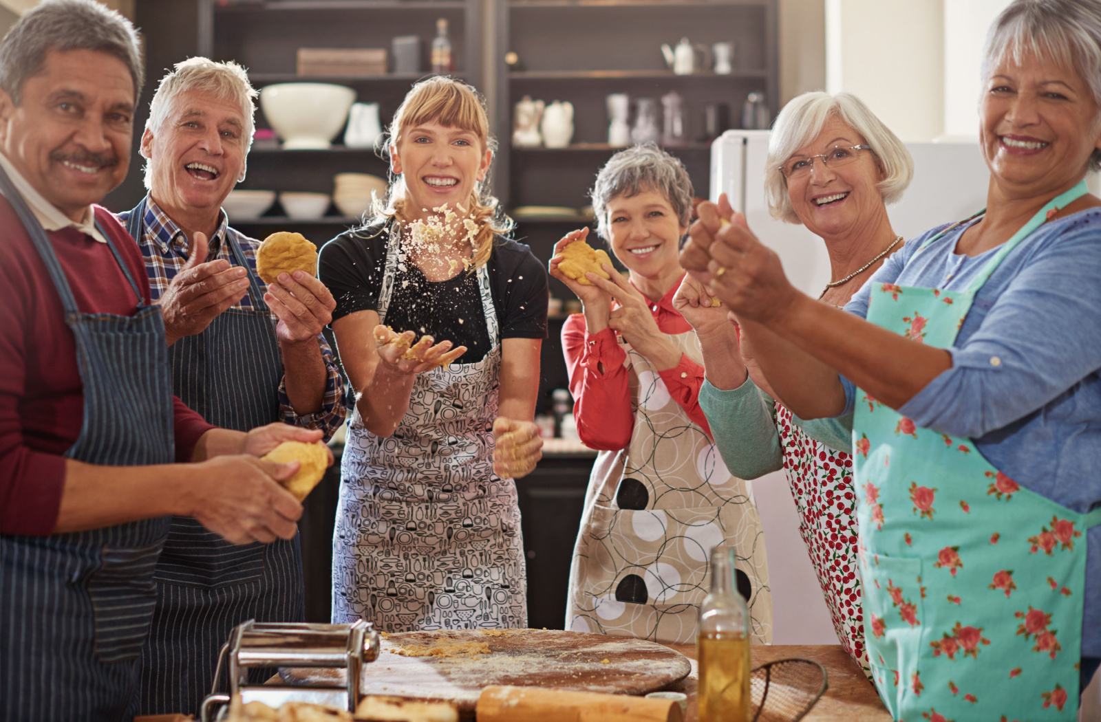 A group of seniors in a baking class with their instructor, each holding dough, smiling and looking directly at the camera.