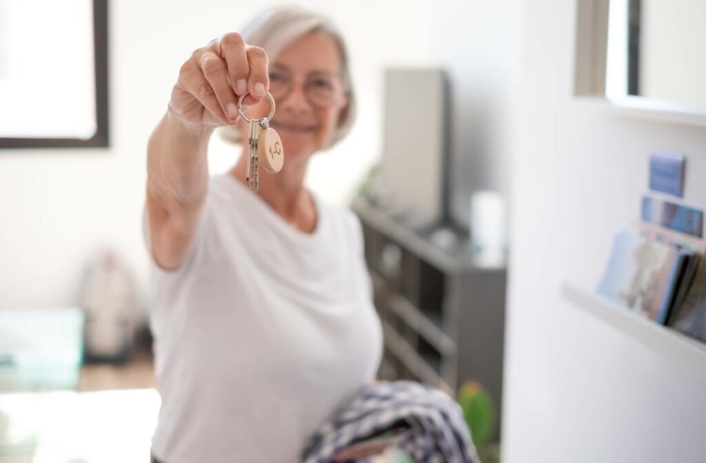 A senior holding their house keys up to the camera and smiling because they were able to get their property taxes deferred.