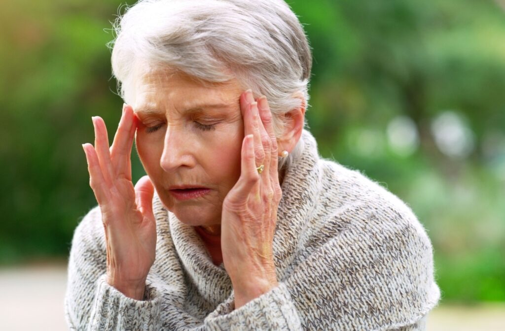 A senior woman experiencing anxiety presses her fingers into her temples with a pained expression.