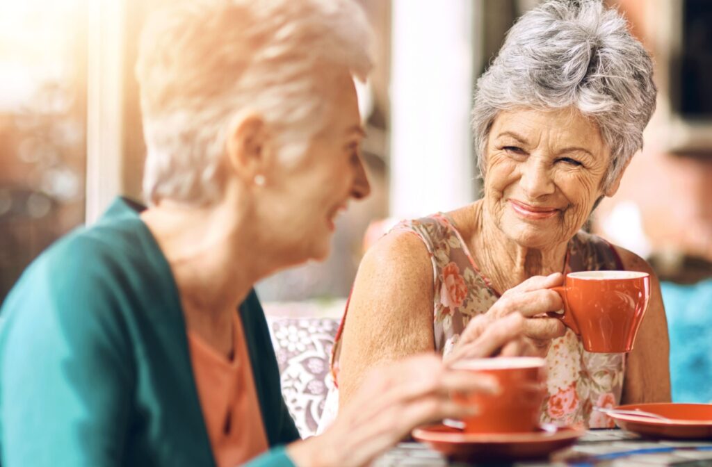 Two elderly women smiling at each other while having a conversation over tea.