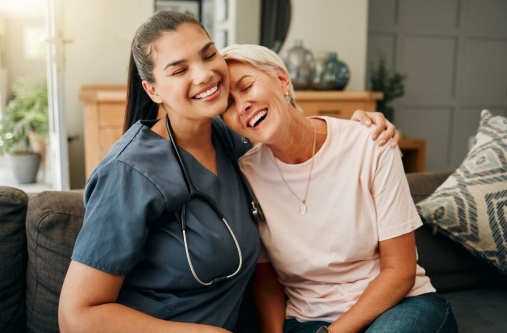 An older adult hugging a smiling caregiver on the couch after a health checkup to practice preventive medicine.