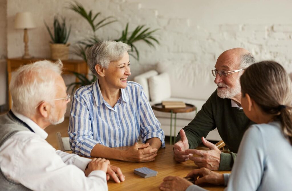 Four seniors sitting around the table talking over a deck of cards and bonding about healthy living and preventive medicine.