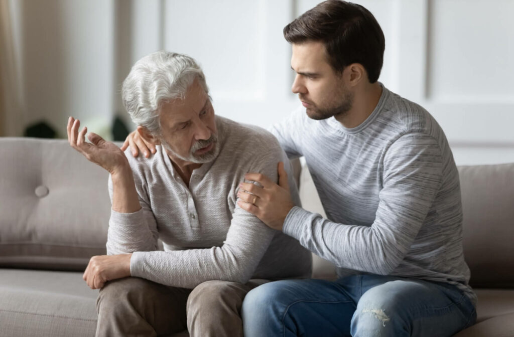 An adult talking with their senior parent on the couch, rubbing their back in support and discussing their worries about malnutrition.