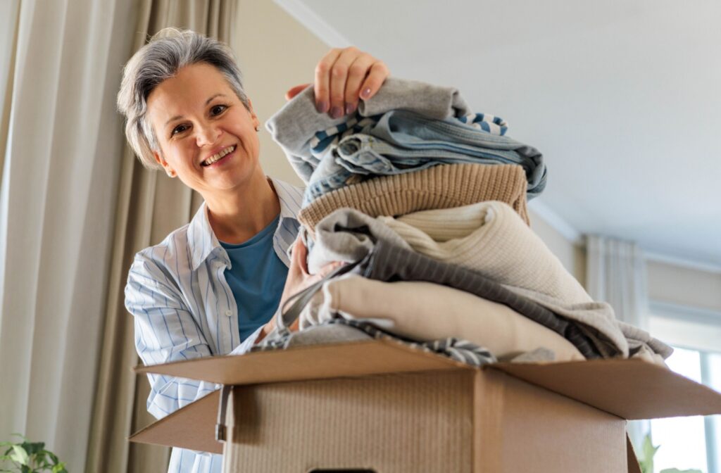 A woman smiling while carefully packing folded clothes into a box, preparing for downsizing or relocation.