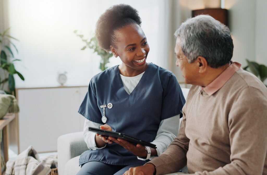 A caregiver holding a tablet and smiling at an older adult while reviewing their care plan together.