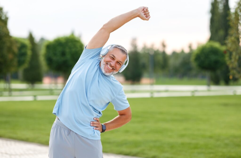 An older adult smiling while stretching outdoors in a park before exercising to improve their cardio health.