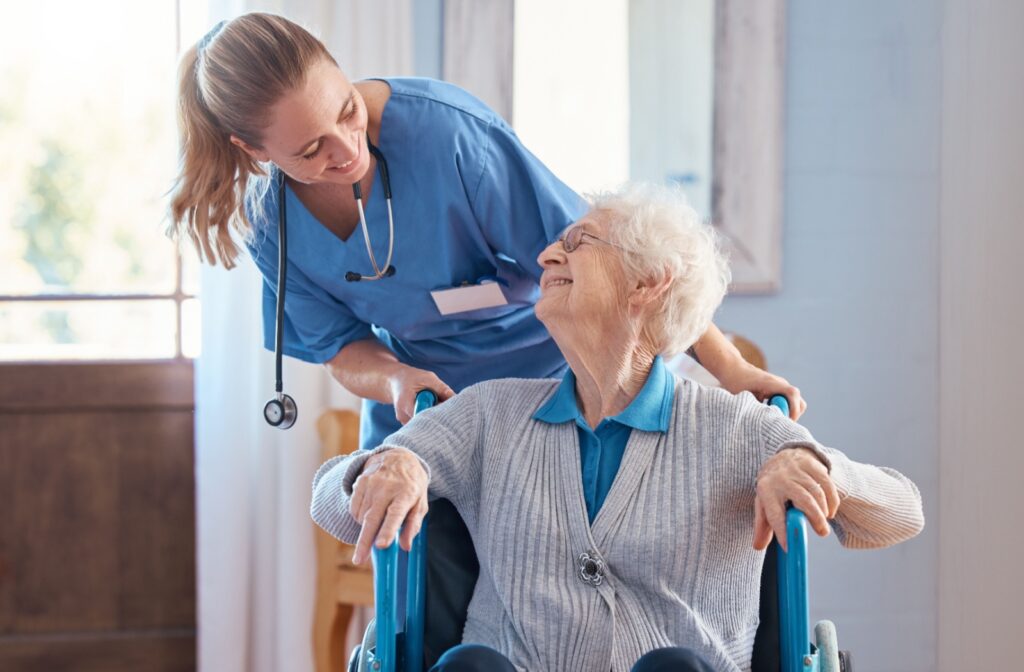 A staff member in a nursing home happily helping an older adult in a wheelchair.