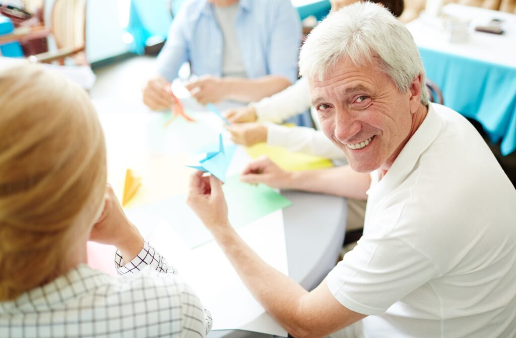 A smiling older adult and a group of older adults doing crafts indoors.