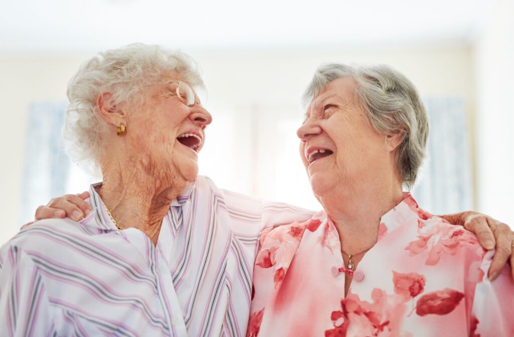Two older friends throw their heads back and laugh with arms around one another