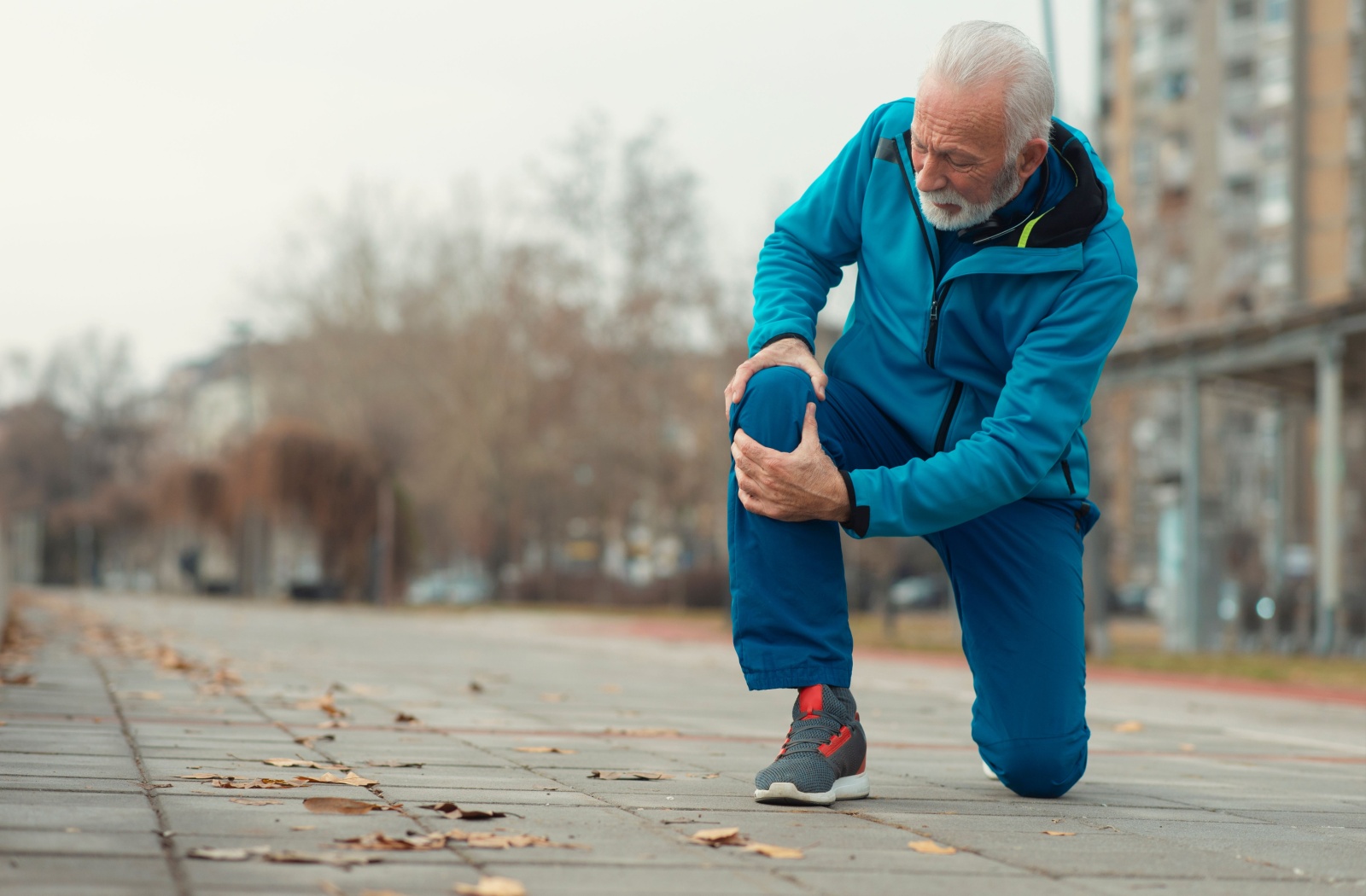 An older person on a walk crouches down and clutches their injured knee.