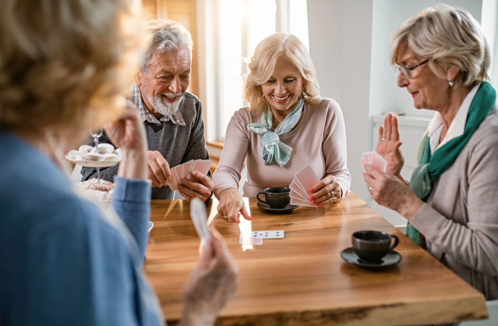 A group of older adults laughing around a table while playing a card game to improve working memory.