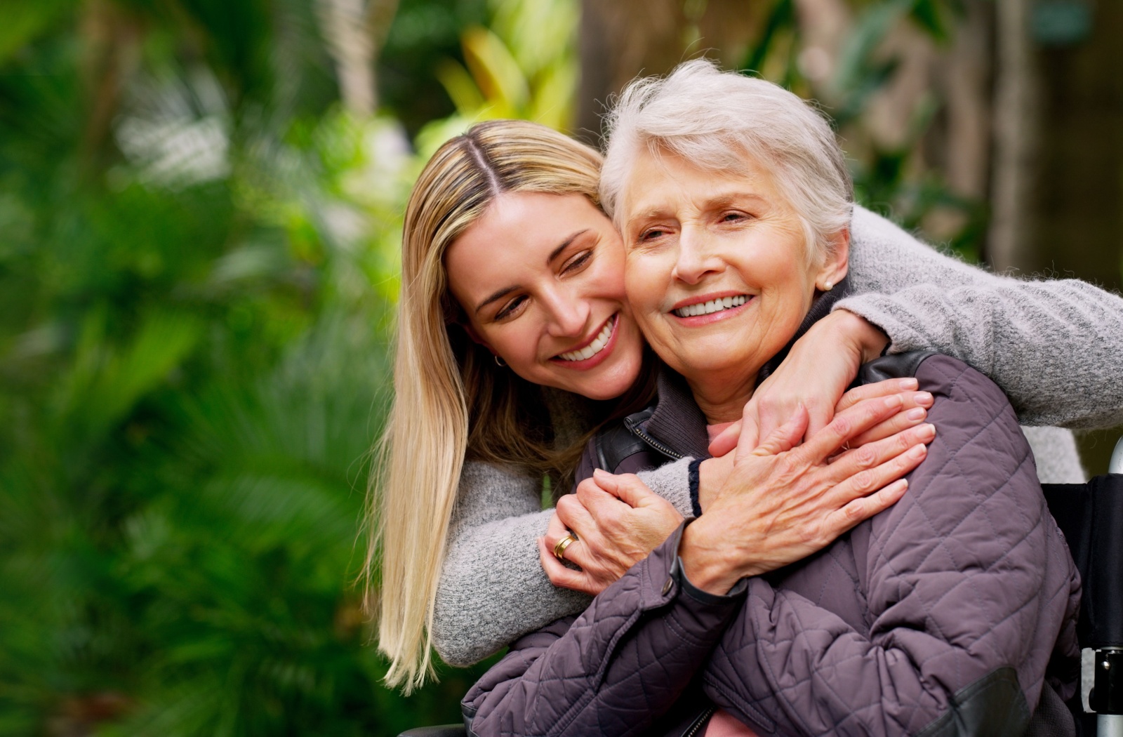 An adult child hugging their older parent from behind during an outdoor walk in assisted living.