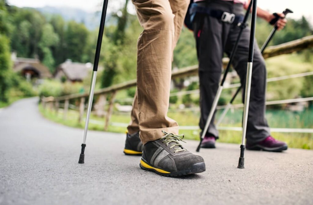 A pair of older adults uses walking poles as they walk a paved path together.