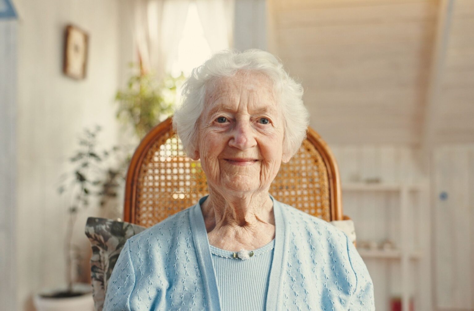 A senior sits and smiles at the camera in assisted living.