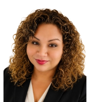 Head-and-shoulders portrait of a woman with curly brown hair, wearing a black blazer and white blouse, smiling at the camera.